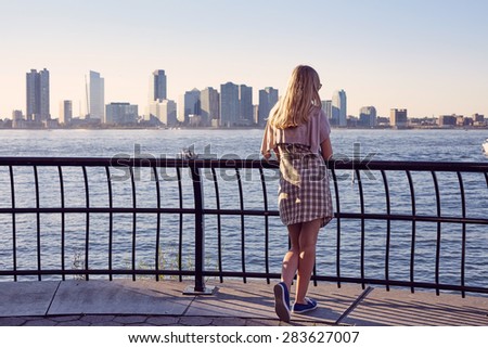 Back view of blonde young woman leaning on berth railing in port on sunny summer day