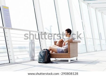 Young smiling man in glasses and headphones sitting on chair in airport departure lounge