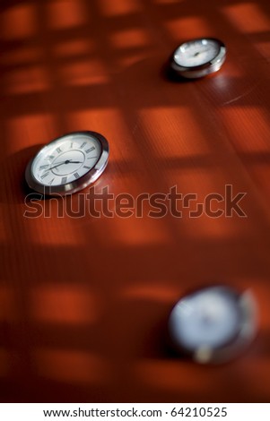 Three clocks on a brown table illuminated by the sun through the blinds.