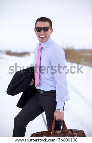 Smiling business man wearing sun-blinkers standing in winter field and holding bag.