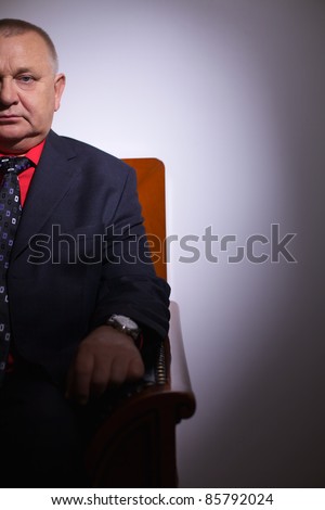 Serious middle aged businessman in suit sitting on leather sofa in office indoor