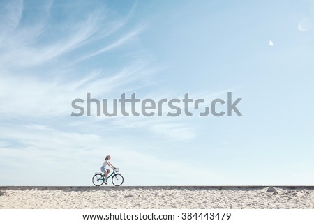 Young woman riding bicycle with basket against blue sky during summer - healthy lifestyle concept