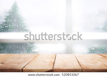 Empty wood table top on blur window view with pine tree in snow fall of winter season background,Table with window glass in the winter morning,For christmas day and new year concept.
