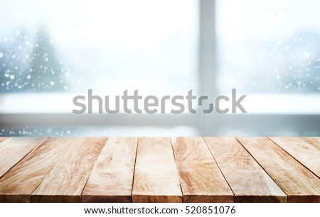 Empty wood table top on blur window view with pine tree in snow fall of morning winter season.For christmas day background and new year concept.