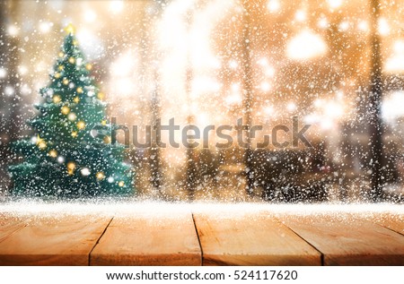 Empty wood table top with snowfall and cafe restaurant in night winter background.For holiday,christmas day and new year concept.