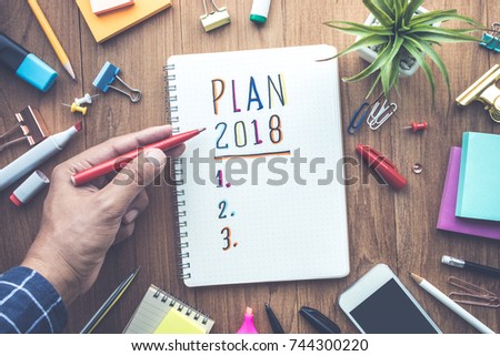 PLAN 2018 message with male hand writing on notepad paper on wooden table and office supplies.Business plan concepts.flat lay design
