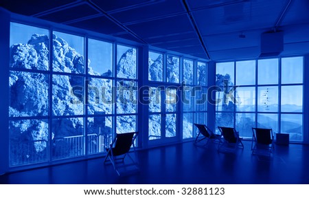 Corporate city background in blue tone. Public space interior with spectacular rocks outside the large scale glass window.