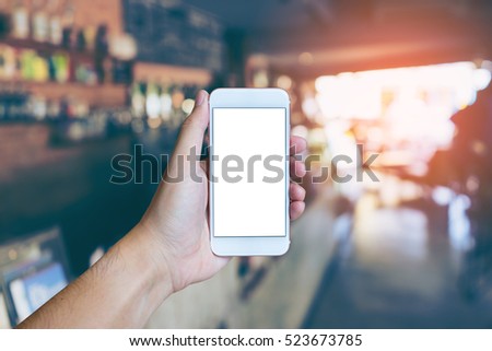 Man\'s hand shows mobile smartphone with white screen in vertical position,  Blurred or Defocus image of Coffee Shop or Cafeteria for use as Background vintage tone. - mockup template and clipping path