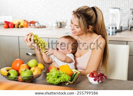 Happy young mother with a baby in the kitchen interior. Fresh vegetables and fruits.