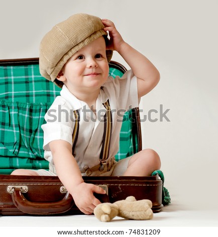 Happy boy sitting in a suitcase. He is wearing a hat. The suitcase is old.