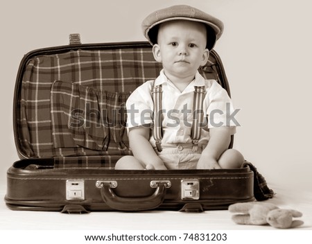 Happy boy sitting in a suitcase. He is wearing a hat. The suitcase is old.
