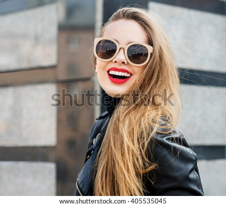 Fashion portrait stylish pretty woman in sunglasses outdoor. Young smiling woman wearing a rock black style having fun in city. Street fashion. Red lipstick.