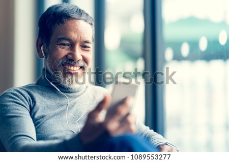 Portrait Smiling Attractive mature man retired with white stylish short beard using smartphone or listening music and sitting at coffee shop cafe.  Old man using social network internet technology