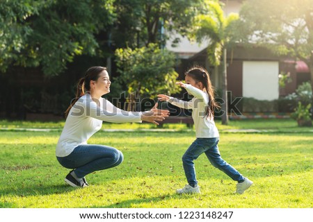 Attractive young asian mother and little cute girl daughter run to hug her mom in garden after back school in evening. Mom and kids feeling relax enjoy playing outside concept. Bonding in asia family.