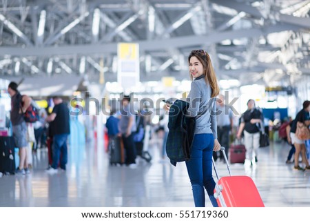 Charming beautiful business woman smile in casual style using smartphone and hold luggage bag for travel with blur the airport terminal.
