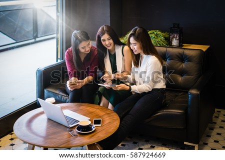 Group of charming  beautiful Asian women using smartphone and laptop, chatting on sofa at cafe, modern lifestyle with gadget technology or working woman on casual business concept