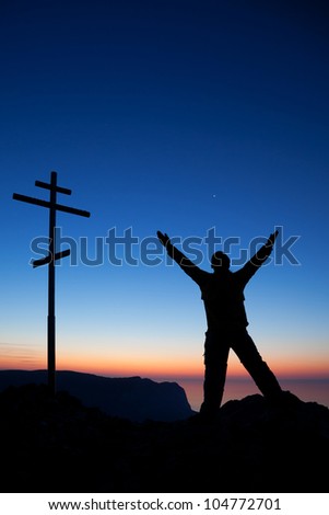 A silhouette of a man near the cross against the sky at sunset