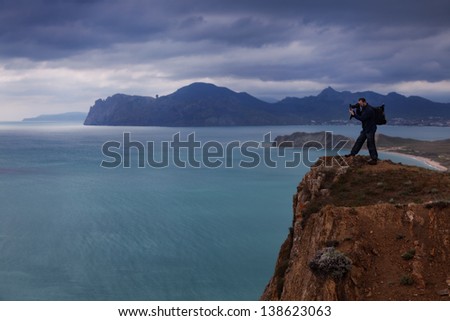 Photographer on the edge of cliff shoots seascape
