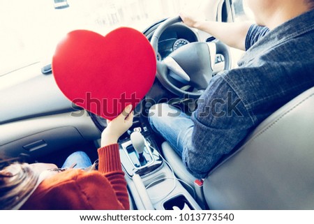 Cheerful couple driving car with heart shape sign, driving safe