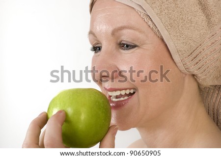 Adult woman with a towel on her head biting an apple. Over white. Not isolated.