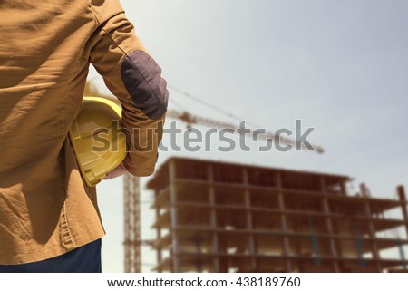worker or engineer holding in hands helmet for workers security on background of new highrise apartment buildings and construction cranes on background.