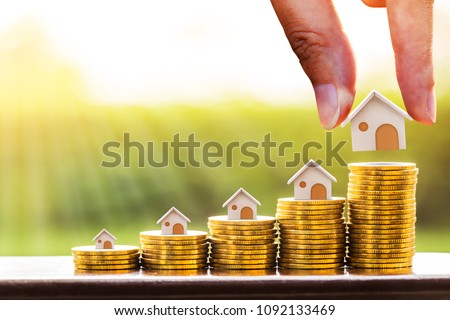 Woman hand hold a wooden home model put on the stack coin with growing in the public park, Savings money for buy house and loan to business investment for real estate concept.
