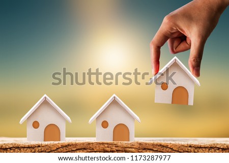 Woman hand hold for select a home model on the wood on sunlight, Loan for real estate or saving money for buy a new house to family in the future concept.