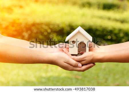 Family home concept, A man and women, hands hold a house made in wood in the public park.