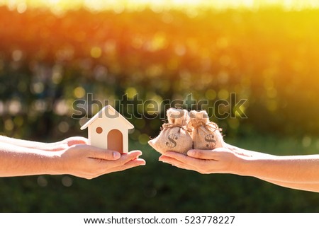 Loans for real estate concept, A man and a women hand holding a money bags and  a model home put together in the public park.