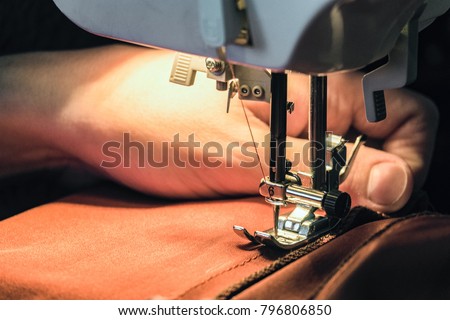Seamstress sews clothes made of red cloth on a sewing machine. Work by the light of the built-in hardware lamp. Steel needle with looper and presser foot close-up.