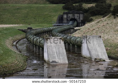 Massive steel water supply pipes leading out of an earth dam reservoir