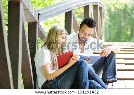Cute couple reading boot while sitting on a wooden bridge outdoors