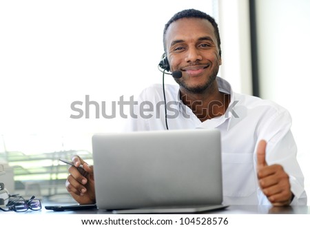 African American young operator with headset and laptop at workplace showing thumb up