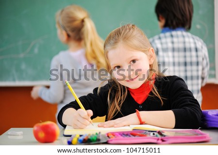 Portrait of a schoolgirl with pencil looking at camera during lesson, friends in background