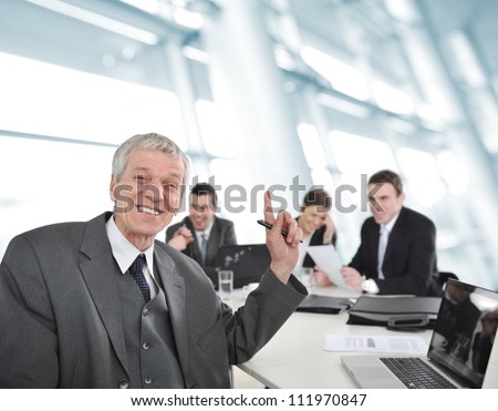 Senior businessman laughing at office meeting and pointing with finger