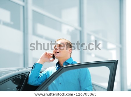 Businessman by the car car, talking on mobile phone, smiling