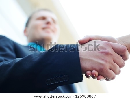 Business people shaking hands. Bright modern building background. Focus on hand.