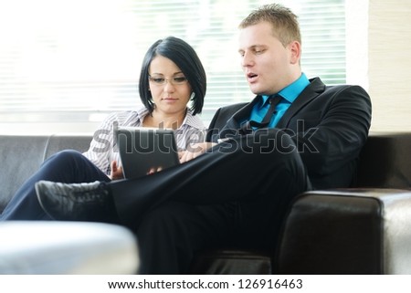 Young businessman and business woman sitting at office lobby on leather sofa working with tablet pc