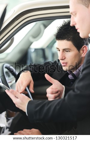 Car seller with car buyer looking at digital tablet