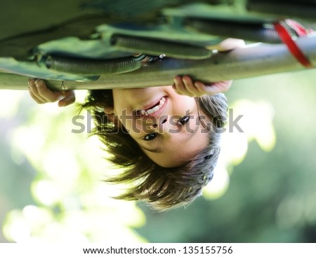 Happy kid outdoors in nature having good time hanging upside down