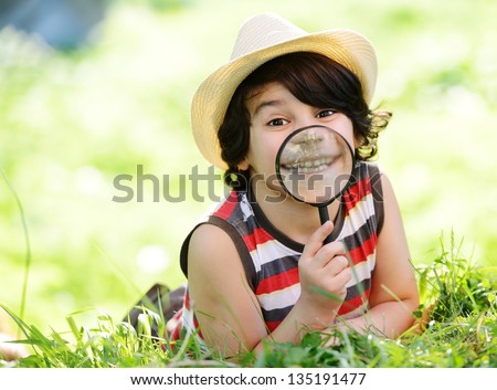 Happy kid with funny big teeth exploring nature using magnifying glass