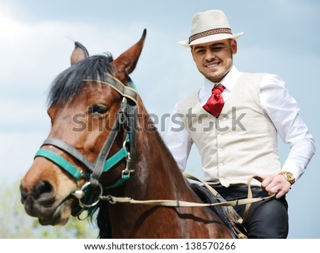 Young stylish man with tie and hat riding a horse on countryside with sky background