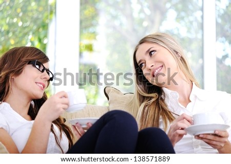 Two beautiful women having conversation drinking coffee and sitting on couch