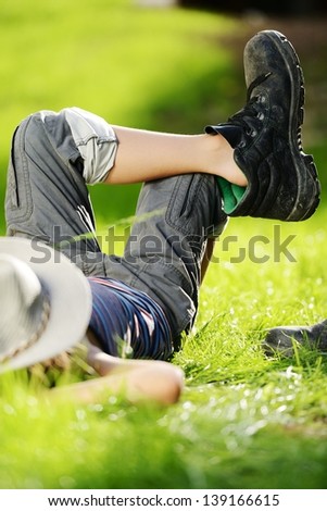 Relaxed kid resting on summer park grass meadow wearing father\'s big shoes