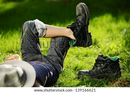 Relaxed kid resting on summer park grass meadow wearing father\'s big shoes