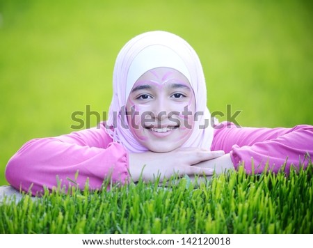 Beautiful teenage Arabic girl lying on green grass in nature