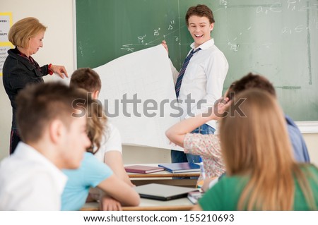 Teacher and student holding a white paper panel in a classroom