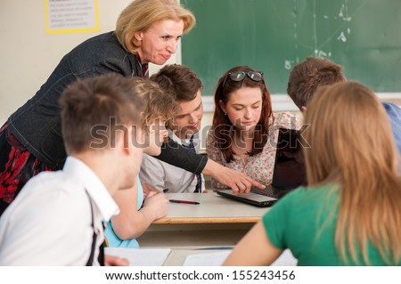 Teacher showing a laptop to a group of her students in a classroom