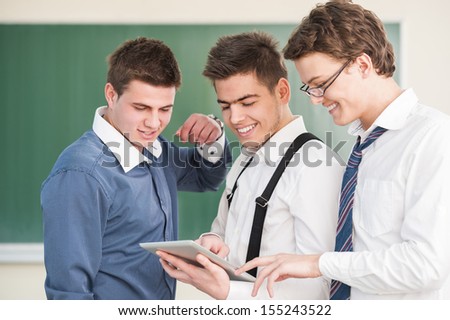 Three smiling students with tablet in front of a chalkboard
