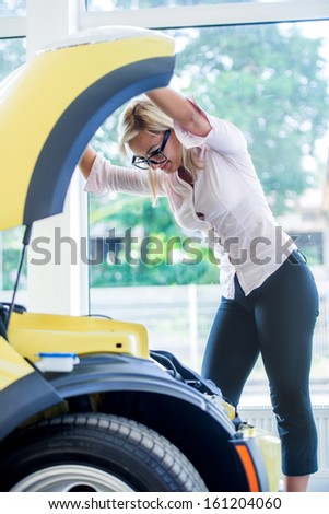 Businesswoman with car trouble looking under the car hood